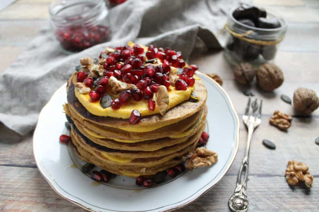 pile of pumpkin pancakes topped with pumpkin cream and pomegranate