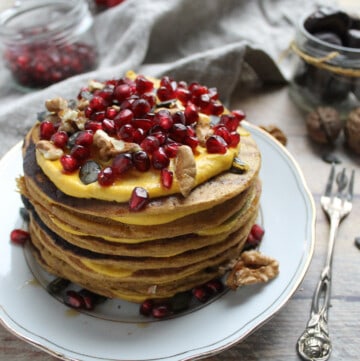 pile of pumpkin pancakes topped with pumpkin cream and pomegranate