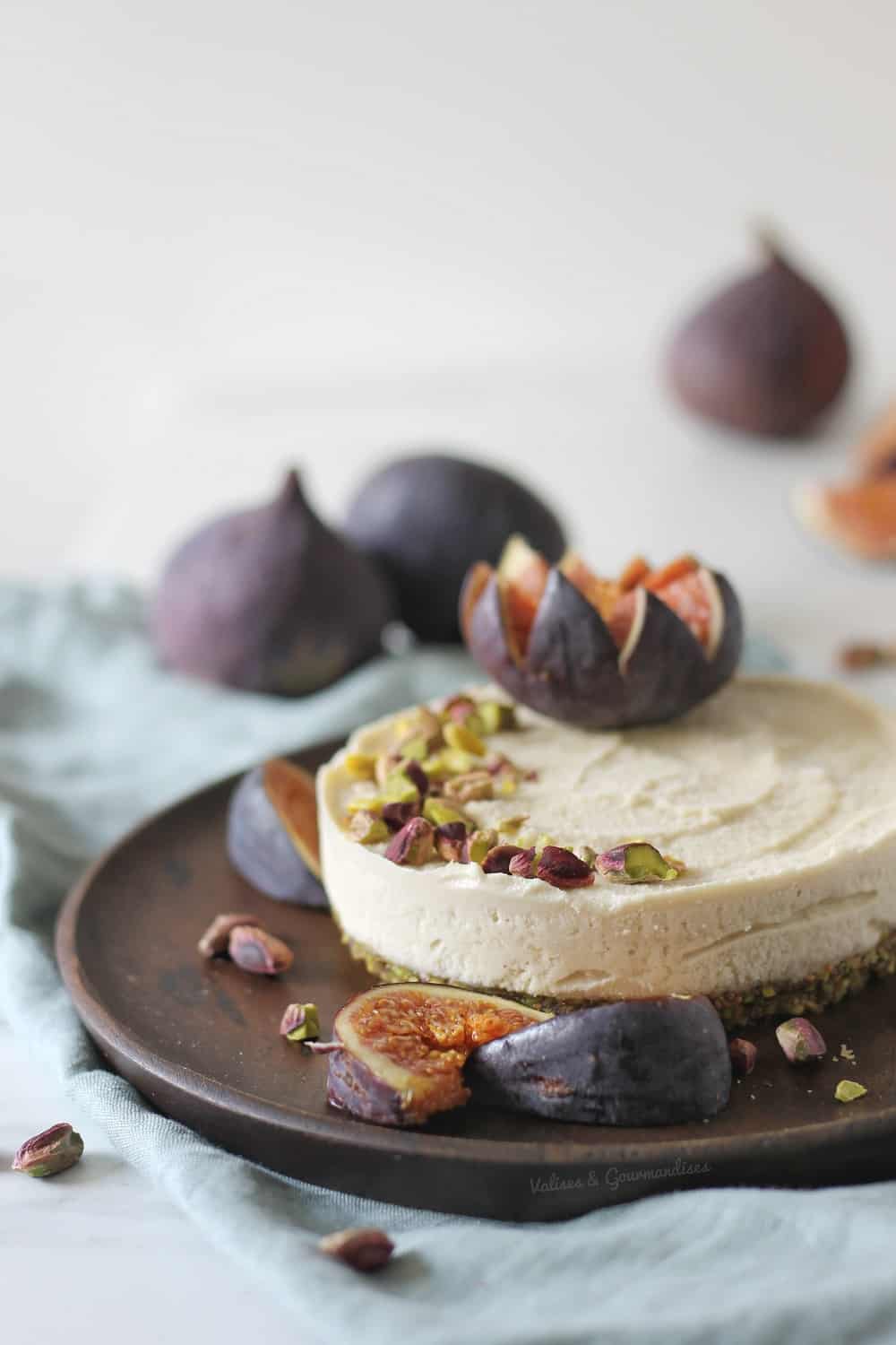 cheesecake vegan fermenté garni de figues fraîches et de pistaches dans une assiette en bois