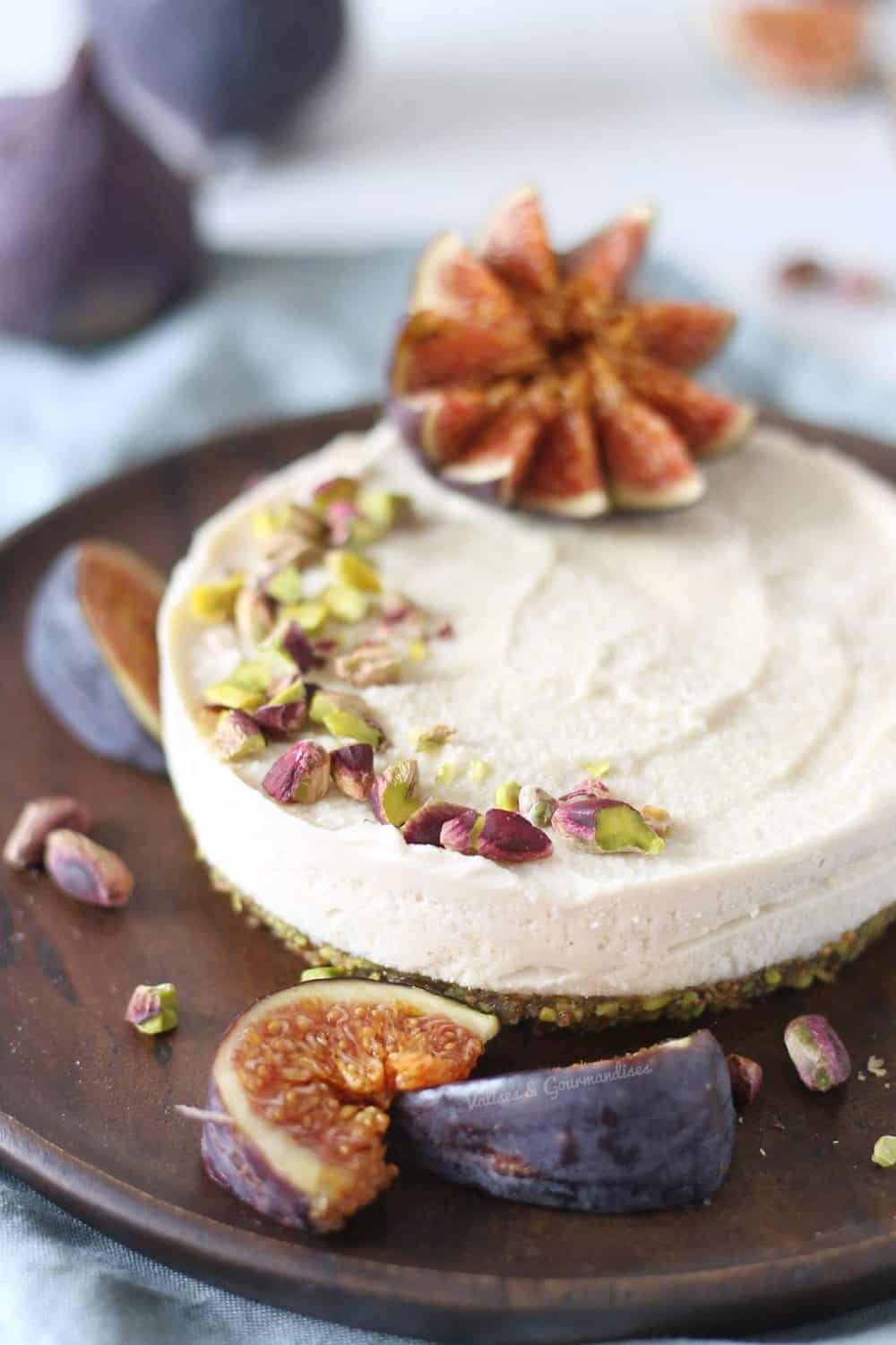 Gâteau au fromage fermenté végane avec figues fraîches et pistaches dans une assiette en bois