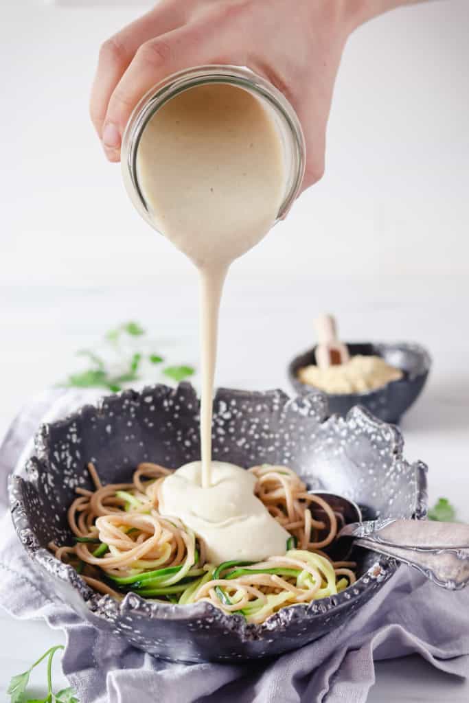 Sauce Alfredo végane versé sur un bol de pâtes au blé entier 