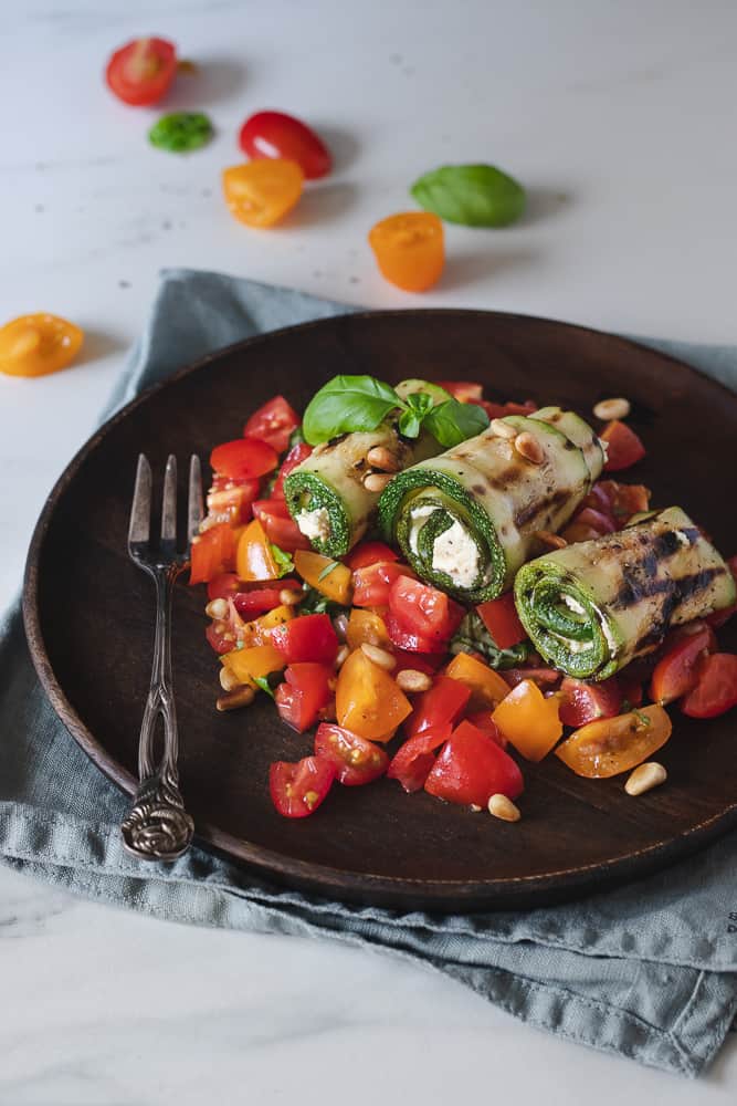 grilled zucchini rolls served on cherry tomato salad, in a wooden plate