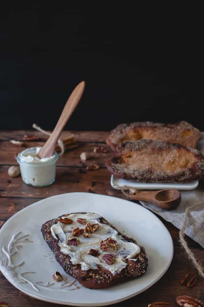 pumpkin beaver tail on a plate with cream cheese frosting and chopped pecans