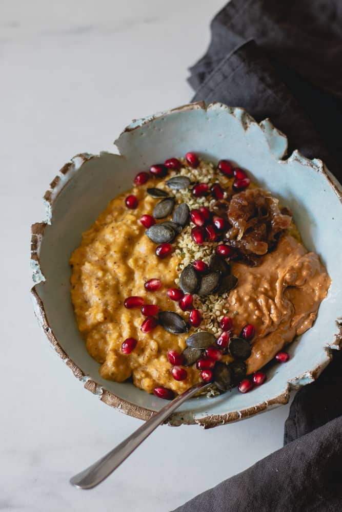 pumpkin oatmeal in blue bowl seen from above, topped with date caramel, cashew butter, pumpkin & hemp seeds and pomegranate